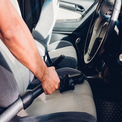 Worker man cleaning dust interior vacuum inside car after wash